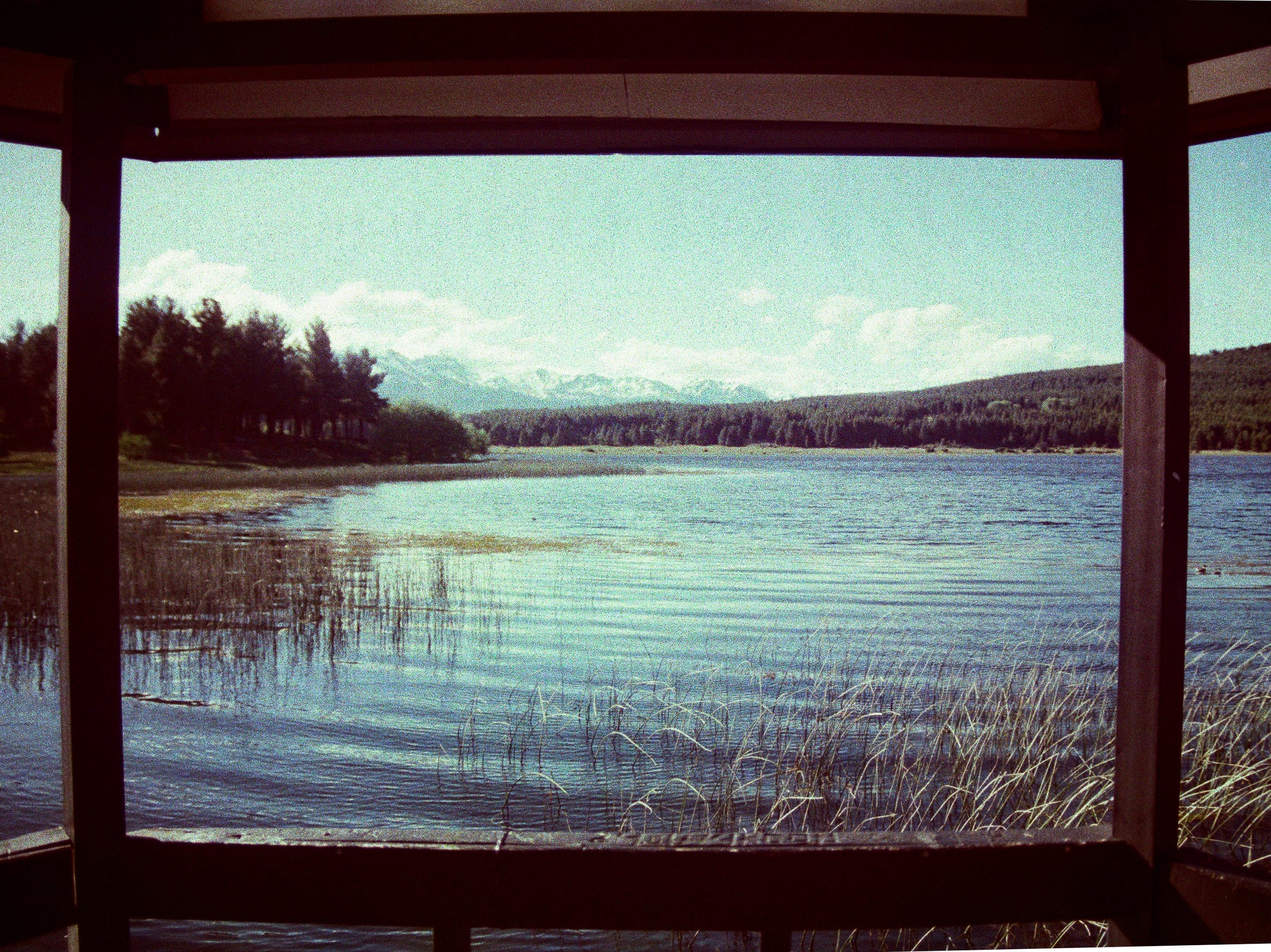 Lake view through a wooden window, mountains and reeds